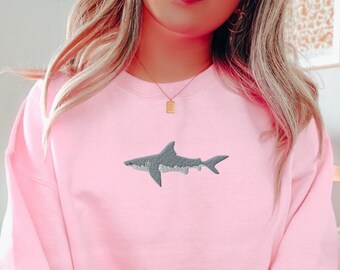 May include: A pink sweatshirt with a gray embroidered shark on the front.