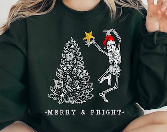 May include: A green sweatshirt with a white graphic of a skeleton wearing a Santa hat and holding a star on top of a Christmas tree. The text "MERRY & FRIGHT" is printed below the graphic.