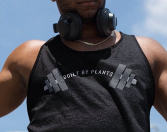 May include: A man wearing a black tank top with the text "BUILT BY PLANTS" and a barbell graphic. He is wearing sunglasses and headphones.