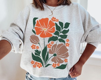 May include: A gray sweatshirt with a floral print featuring orange, brown, and green flowers. The flowers are stylized and have a vintage aesthetic.