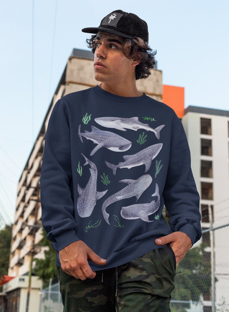 May include: A navy blue sweatshirt with a pattern of whale sharks and seaweed. The sweatshirt has long sleeves and a crew neck.