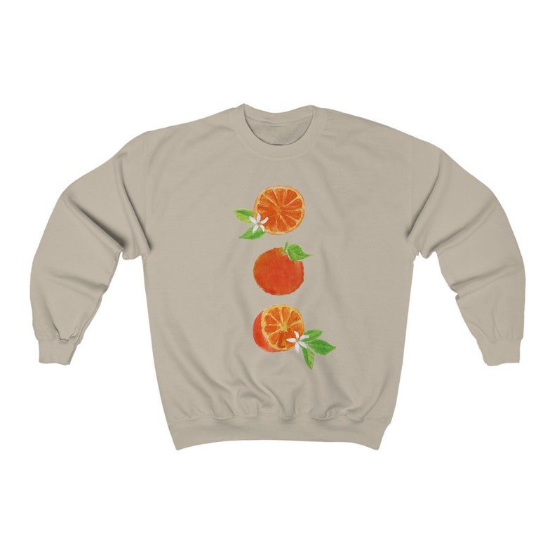 May include: A beige sweatshirt with a graphic of three orange slices with green leaves and white flowers.