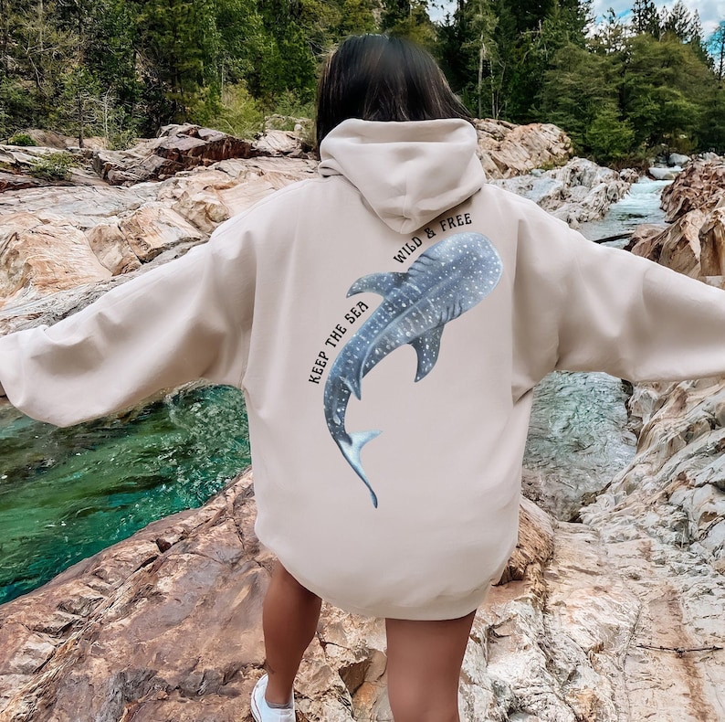 May include: A beige hoodie with a whale shark graphic on the back. The graphic says "Keep the Sea Wild & Free".