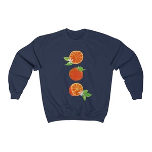 May include: Navy blue sweatshirt with a graphic of three orange slices with white blossoms and green leaves.