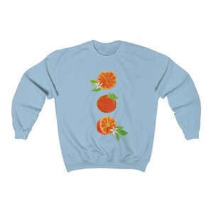 May include: A light blue sweatshirt with a vertical design of three orange slices with white blossoms and green leaves.