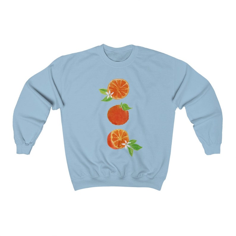 May include: A light blue sweatshirt with a vertical design of three orange slices with white blossoms and green leaves.