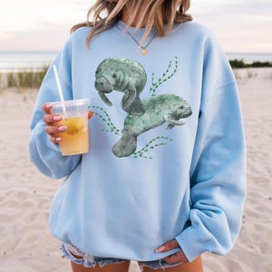 Two large watercolor manatees and seaweed on the front of a sweatshirt