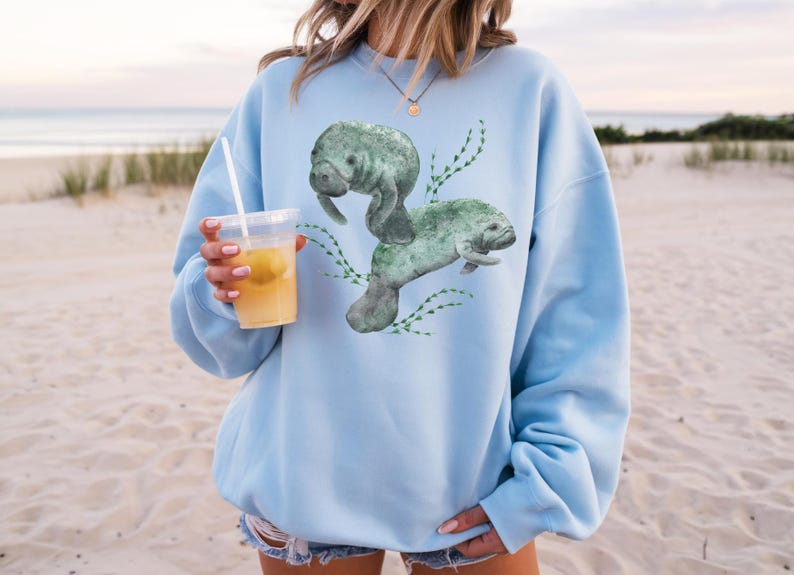 Two large watercolor manatees and seaweed on the front of a sweatshirt