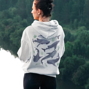 May include: A white hoodie with a graphic print of multiple whale sharks and seaweed on the back. The hoodie has a drawstring hood and a kangaroo pocket.