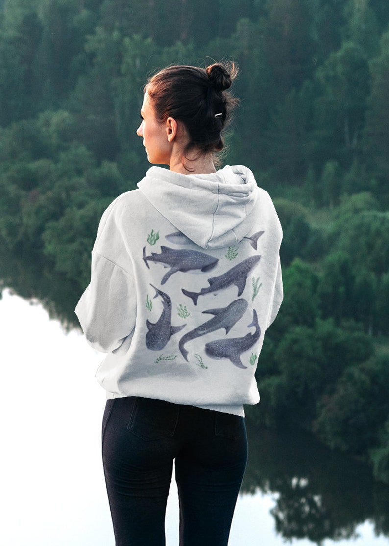 May include: A white hoodie with a graphic print of multiple whale sharks and seaweed on the back. The hoodie has a drawstring hood and a kangaroo pocket.