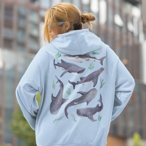 May include: A light blue hoodie featuring a graphic print of several whale sharks in different positions. The sharks are surrounded by green seaweed.