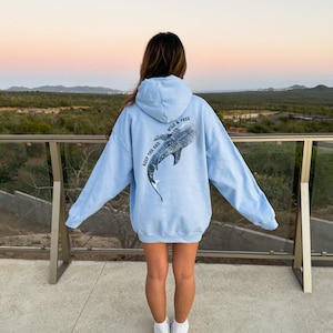 May include: A light blue hoodie with a graphic of a whale shark on the back. The text "Keep the Sea Wild & Free" is printed on the hoodie.