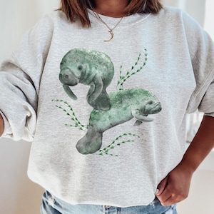 Two large watercolor manatees and seaweed on the front of a sweatshirt