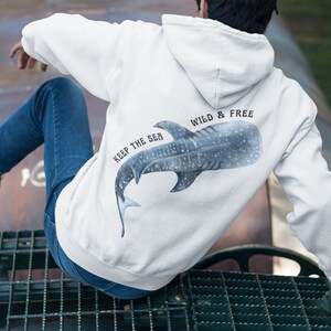 May include: White hoodie with a blue whale shark graphic on the back. The text "Keep the Sea Wild & Free" is printed on the hoodie.