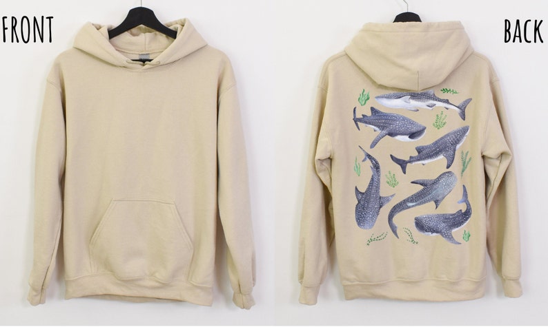 May include: A beige hoodie with a front pocket. The back of the hoodie features a design of multiple whale sharks in a light blue and grey colour scheme with green seaweed.
