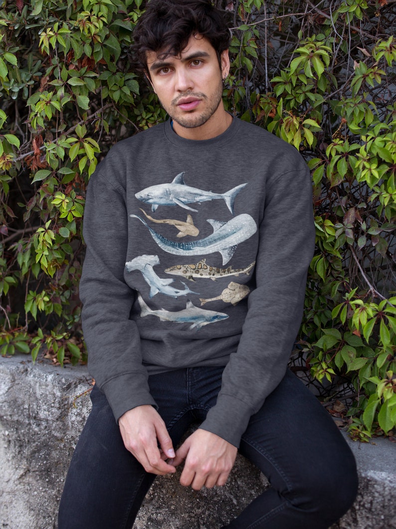 May include: A dark grey sweatshirt featuring a graphic print of various sharks and rays. The print includes a hammerhead shark, a whale shark, and a manta ray.