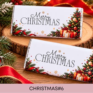 May include: Two rectangular chocolate bars wrapped in white paper featuring the text Merry CHRISTMAS in black script and serif font. The design includes a decorated Christmas tree, wrapped gifts, pine branches, and small gold snowflakes.