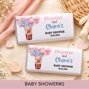 May include: Two rectangular chocolate bars wrapped in white paper featuring a watercolour illustration of a teddy bear in a hot air balloon with pink and blue balloons. The text reads Praveeni and Chami's BABY SHOWER 01.02.2026 in pink and blue.