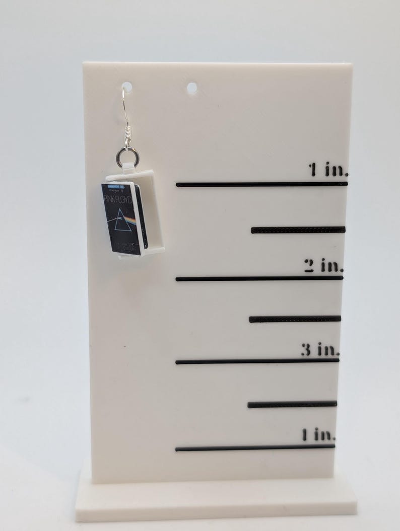 a pair of earrings sitting on top of a white stand