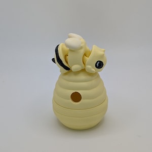 May include: A yellow ceramic bee figurine perched on top of a yellow ceramic beehive with a hole in the center.