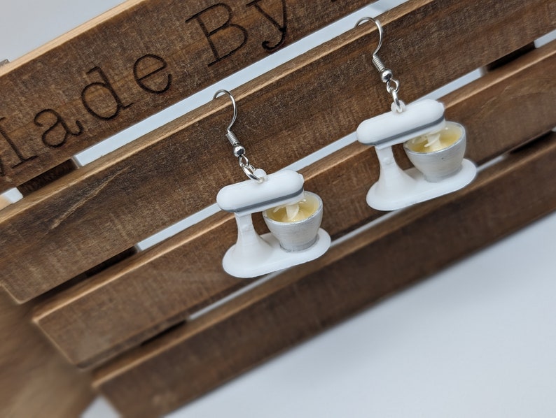 May include: A pair of white and silver stand mixer earrings. The earrings are made of polymer clay and have a realistic look.