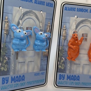 May include: Novelty earrings with blue mouse and orange bear charms. The earrings are nickel-free and have silver-coloured hooks. The text "ALWAYS RANDOM. ALWAYS WEIRD." is printed at the top of the card. The shop name "BY MADA" and Etsy shop URL are printed at the bottom.