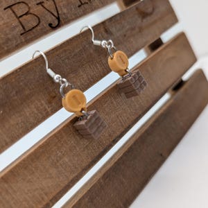 May include: A pair of silver dangle earrings with a brown and tan chocolate bar charm and a gold charm with the number "1" on it.