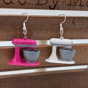 May include: A pair of earrings featuring miniature stand mixer designs. One earring is pink with a gray bowl, and the other is white with a gray bowl.