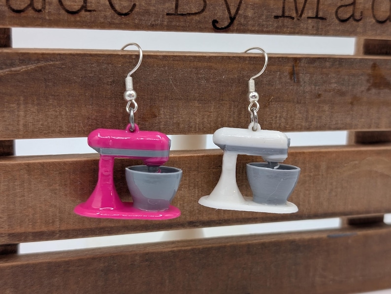 May include: A pair of earrings featuring miniature stand mixer designs. One earring is pink with a gray bowl, and the other is white with a gray bowl.