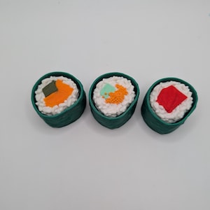 Könnte beinhalten: Drei grüne Sushi-Rollen mit verschiedenen Füllungen. Die erste Rolle hat einen Belag aus grünem Seetang, die zweite hat orangefarbene Fischeier und die dritte hat einen roten Fischbelag.