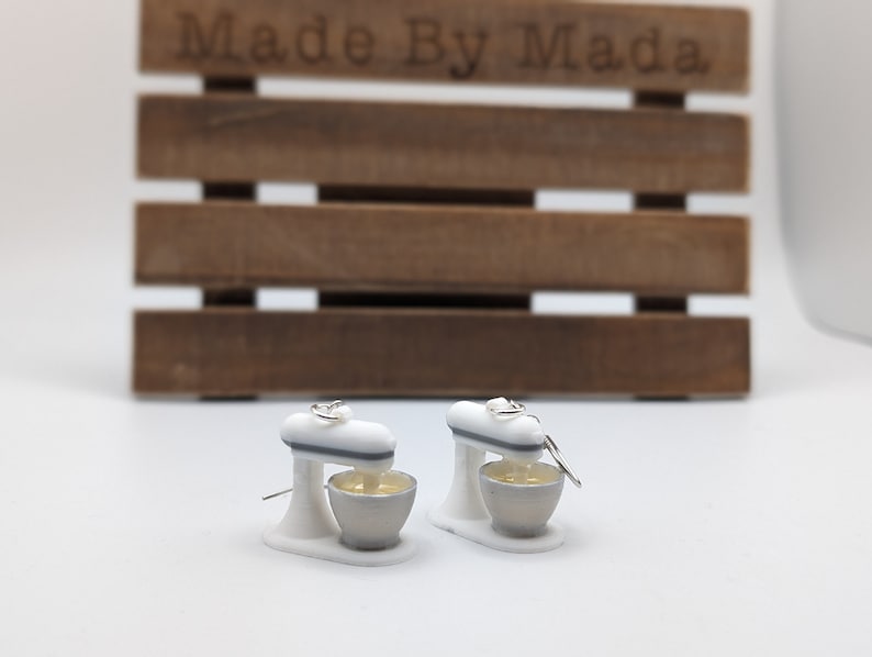 May include: A pair of white and gray miniature stand mixer earrings. The earrings are made of polymer clay and have a silver hook.