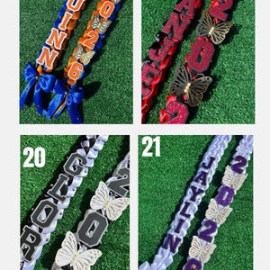 May include: Four graduation leis with names and the year 2026. The leis are in various colors, including blue, red, black, and white, and are decorated with butterfly accents and bows. Each lei has a different name.