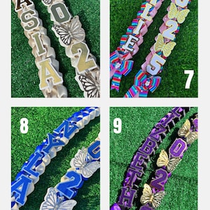 May include: A collection of graduation leis with names and the year 2022. Each lei features a different color scheme, butterfly accents, and the name of the graduate. The leis are displayed on a green background.