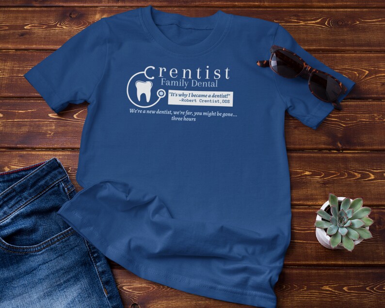 May include: A blue t-shirt with a white graphic design that says "Crentist Family Dental" and includes a quote: "It's why I became a dentist!" -Robert Crentist, DDS. The graphic also includes a tooth and a stethoscope.