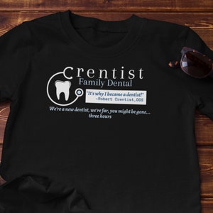 May include: Black t-shirt with a white graphic of a tooth and a stethoscope. The text "Crentist Family Dental" is written in white above the graphic. The text "It's why I became a dentist! -Robert Crentist, DDS" is written in blue below the graphic. The text "We're a new dentist, we're far, you might be gone... three hours" is written in white below the blue text.