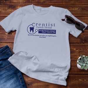 May include: A light blue t-shirt with a blue and white logo that says "Crentist Family Dental" and the text "It's why I became a dentist! -Robert Crentist, DDS We're a new dentist, we're far, you might be gone... three hours".