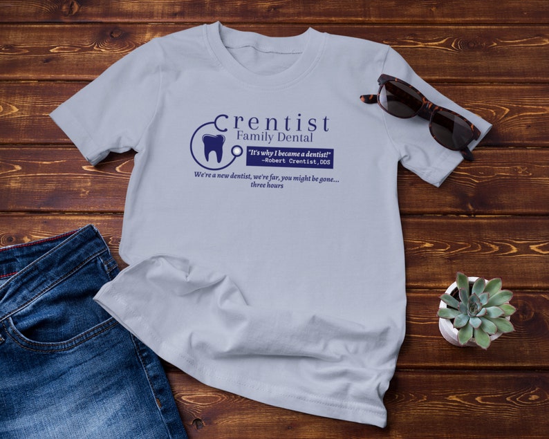 May include: A light blue t-shirt with a blue and white logo that says "Crentist Family Dental" and the text "It's why I became a dentist! -Robert Crentist, DDS We're a new dentist, we're far, you might be gone... three hours".