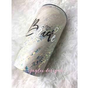May include: A white tumbler with a glittery finish and a black and silver vinyl design that says "Bride" with a diamond symbol.