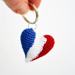 May include: A crocheted heart-shaped keychain in red, white, and blue colors. The keychain is attached to a silver key ring.