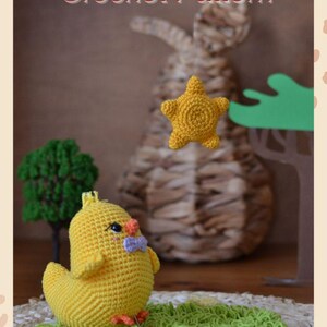 Puede incluir: Un pollito amarillo tejido a ganchillo con una pajarita azul est&aacute; sentado sobre una superficie verde tejida a ganchillo. Una estrella amarilla y un peque&ntilde;o &aacute;rbol verde est&aacute;n en el fondo. El texto "The Bright Sun Crochet Pattern" est&aacute; en la parte superior, con "English Version" en la parte inferior.