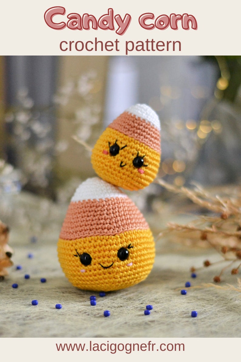May include: Two crocheted candy corn toys with smiling faces. The larger candy corn is orange, yellow, and white. The smaller candy corn is stacked on top of the larger one. The candy corn toys are on a blue and white surface.