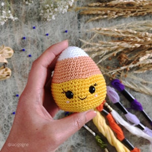 May include: A crocheted candy corn toy with a white top, orange middle, and yellow bottom. The toy has a smiling face with black eyes and a black mouth.