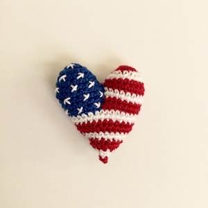 May include: A crocheted heart-shaped ornament in the colors of the American flag. The heart is red, white, and blue with white stars on a blue field.
