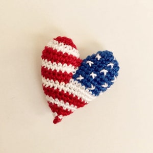 May include: A crocheted heart-shaped ornament in the colors of the American flag. The heart is red, white, and blue with white stars on the blue side.