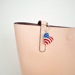 May include: A pink tote bag with a red, white, and blue crocheted heart-shaped keychain attached to the zipper pull.