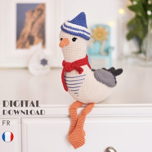 Può includere: Un gabbiano all'uncinetto con un cappello da marinaio a righe blu e bianche e una sciarpa rossa. Il gabbiano è seduto su una superficie bianca. DOWNLOAD DIGITALE FR