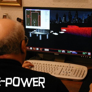 May include: A person is sat in front of a computer playing a video game. The game is displayed on the computer screen and shows a city skyline, a red bridge, and several fish swimming. The text "BRANE-POWER" is visible at the bottom of the image.