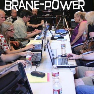 May include: A group of people are sitting at a table working on laptops. The table is covered in a white tablecloth and there are several water bottles on the table. The text "Brane-Power" is visible in the background.