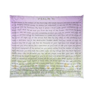 Puede incluir: Una almohada rectangular con el texto del Salmo 91 impreso en negro. El texto está rodeado por un diseño floral morado y blanco sobre un fondo morado claro. La almohada tiene un borde morado.