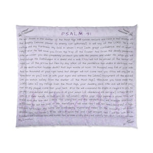 Puede incluir: Una almohada cuadrada de color blanquecino con el texto del Salmo 91 impreso en un estilo manuscrito. El texto es negro, con el título "SALMO 91" en morado. Diseños florales en las esquinas.